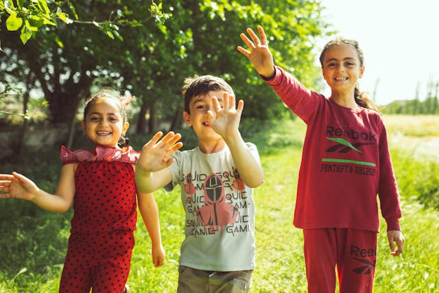 Inclusive Summer Camp children outdoors in a sunny grassy park area with trees in the background